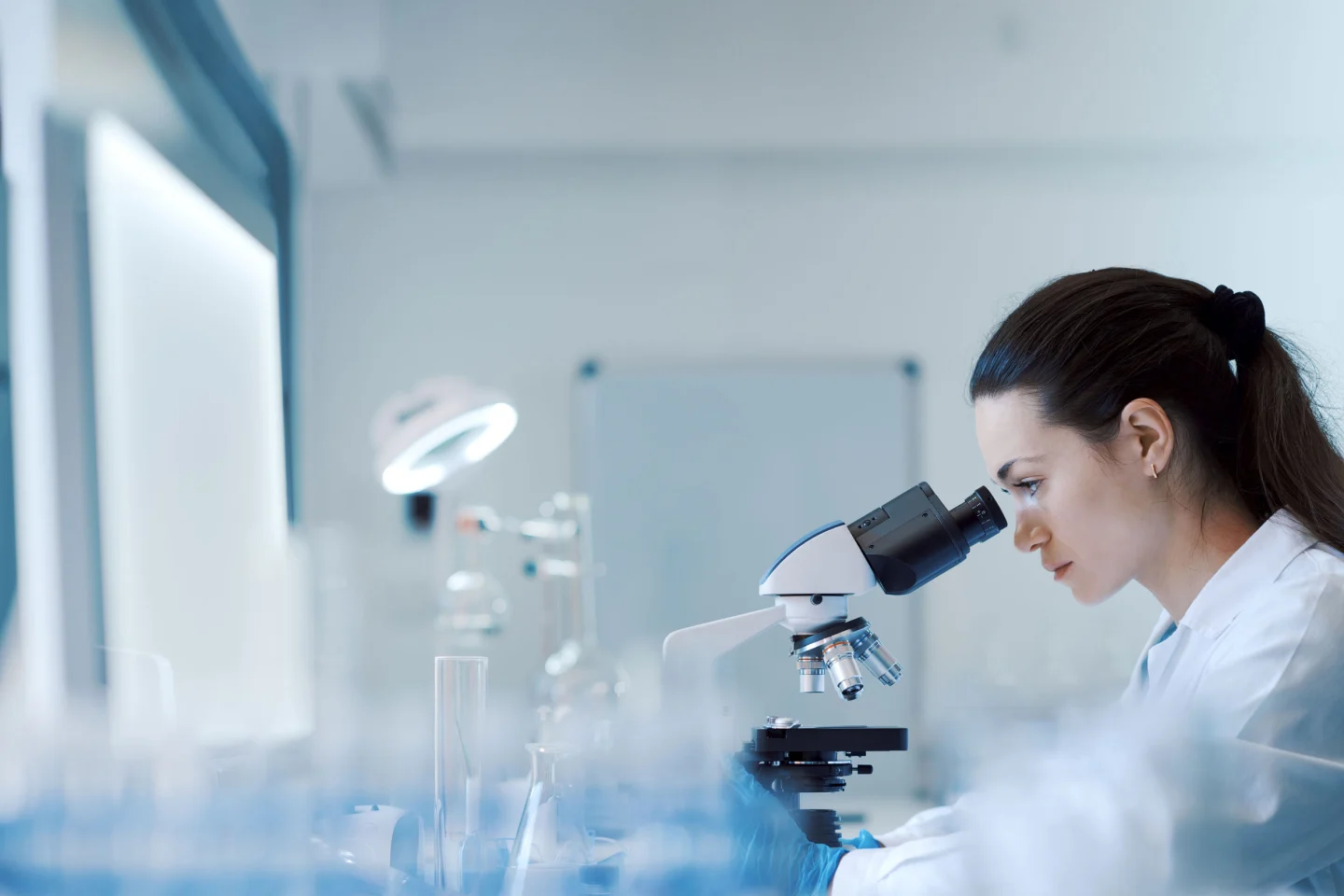 Scientifique en blouse blanche observant un échantillon au microscope dans un laboratoire d'analyses